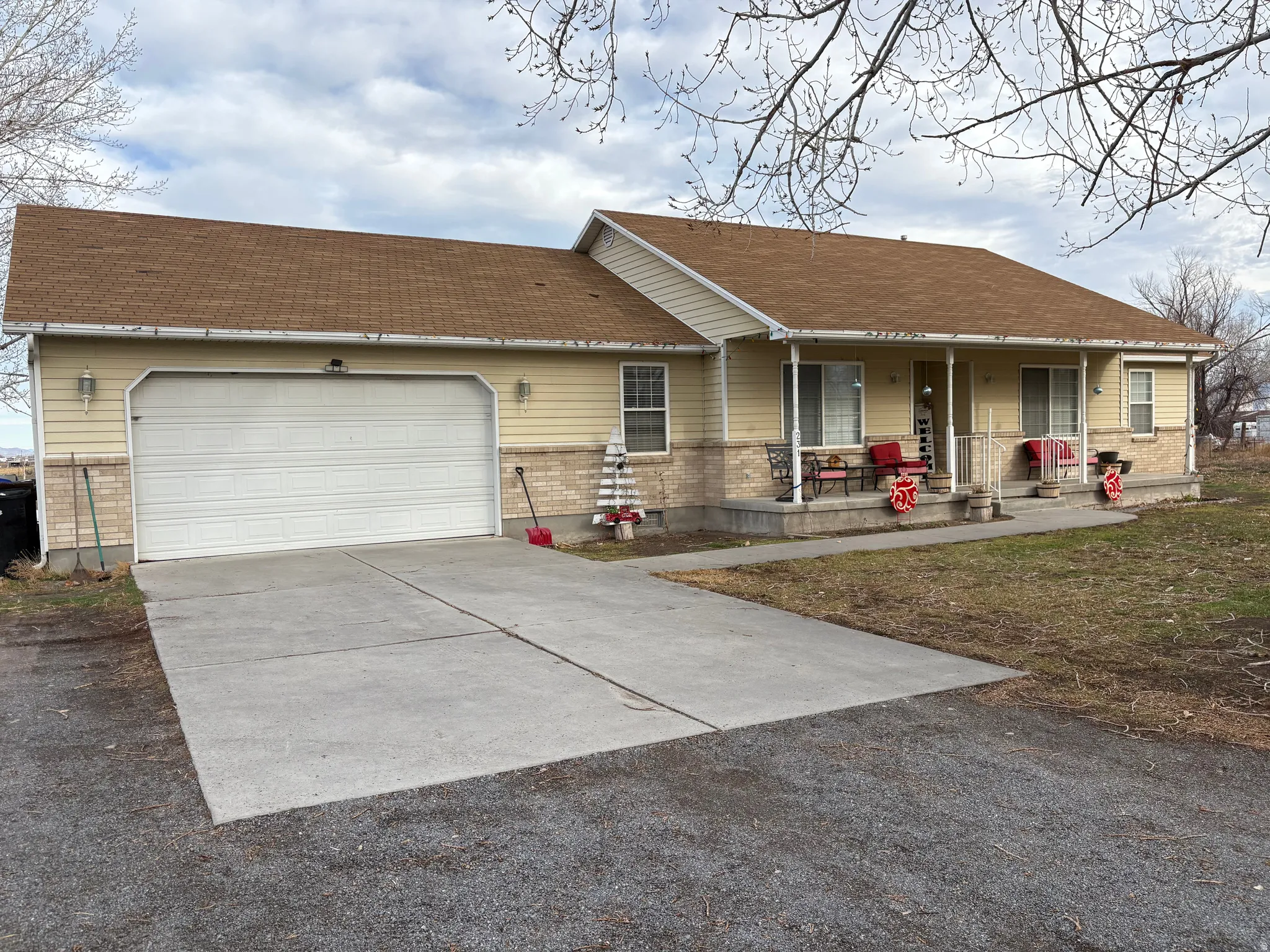 Single story home featuring concrete driveway, covered porch, a garage, brick siding, and a shingled roof