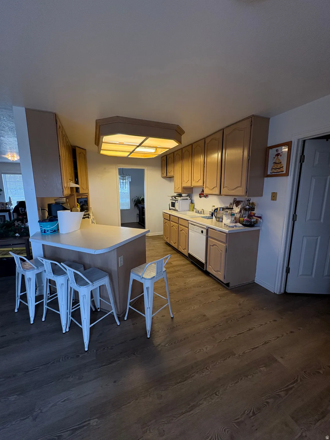Kitchen with light countertops, a breakfast bar area, dark wood-style floors, a peninsula, and white dishwasher