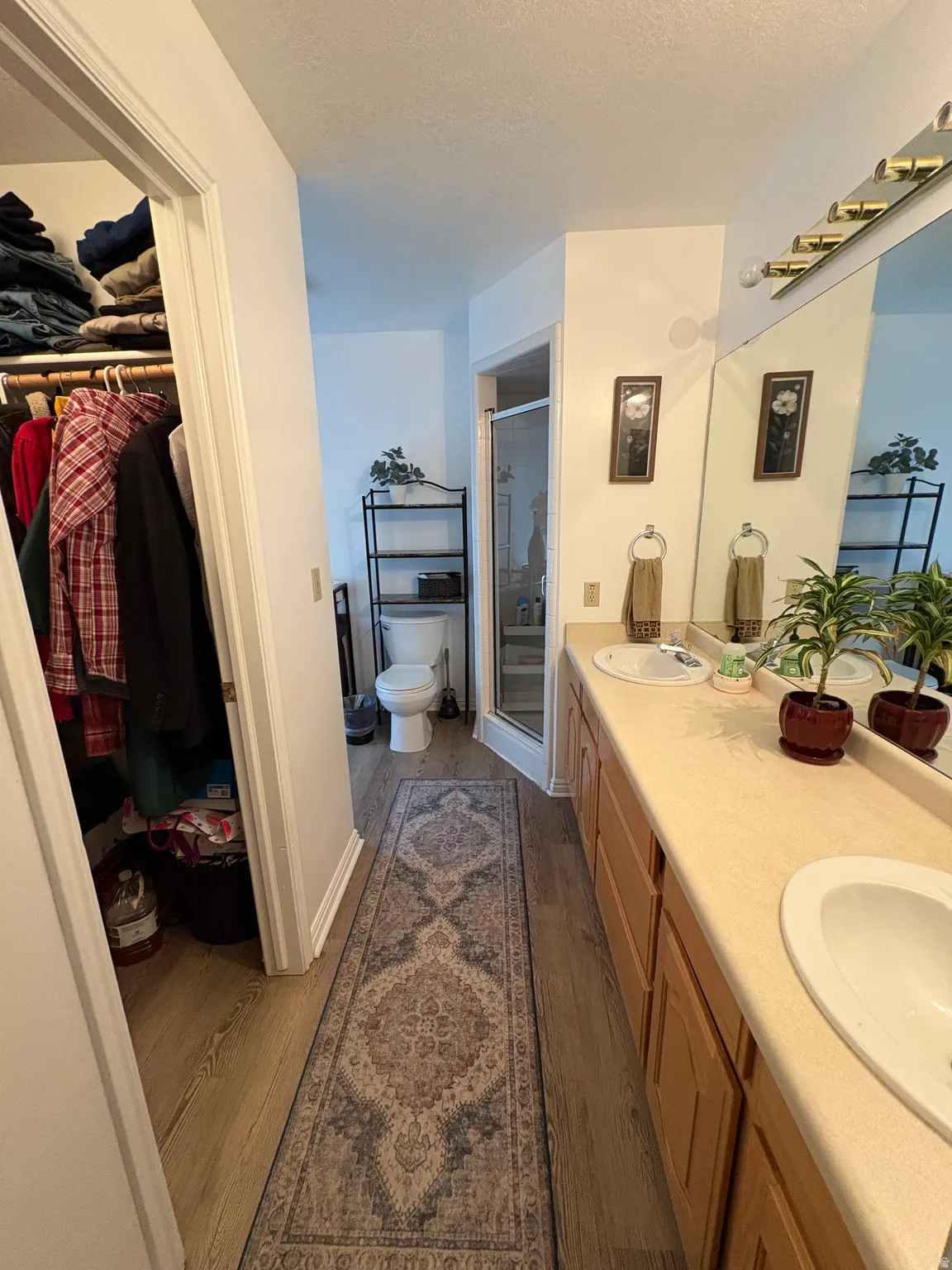 Bathroom with a walk in closet, a stall shower, dark wood finished floors, double vanity, and a textured ceiling