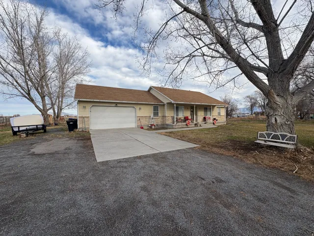 Single story home featuring driveway, a garage, covered porch, a shingled roof, and a front lawn
