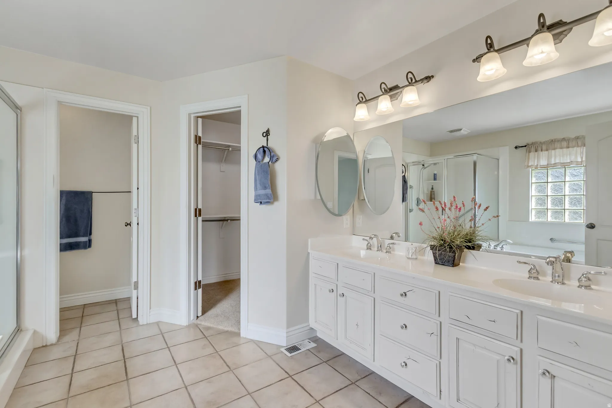 Bathroom featuring a stall shower, double vanity, a walk in closet, light tile patterned floors, and a garden tub