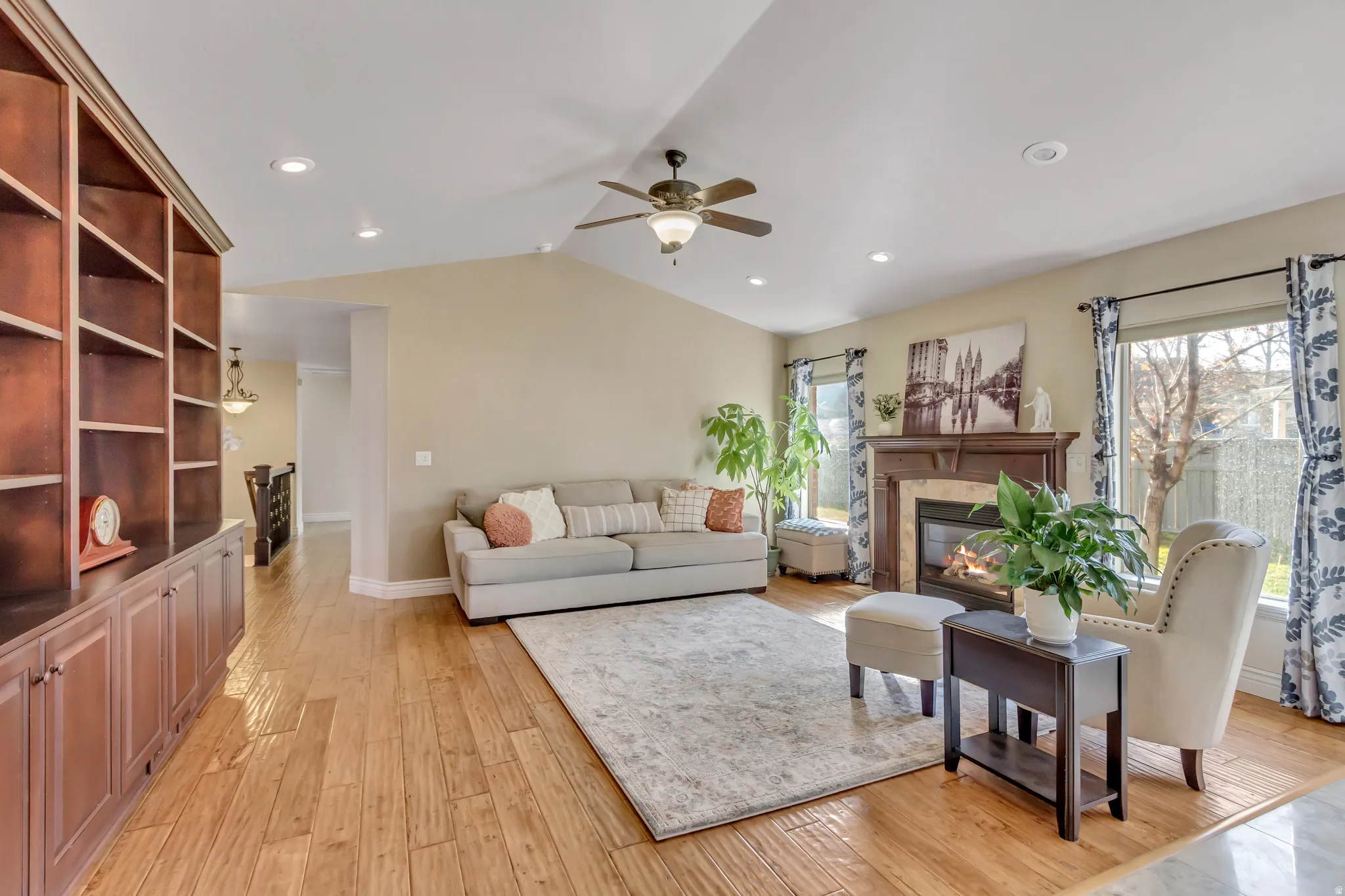 Living room featuring vaulted ceiling, light wood-type flooring, a fireplace, a ceiling fan, and recessed lighting
