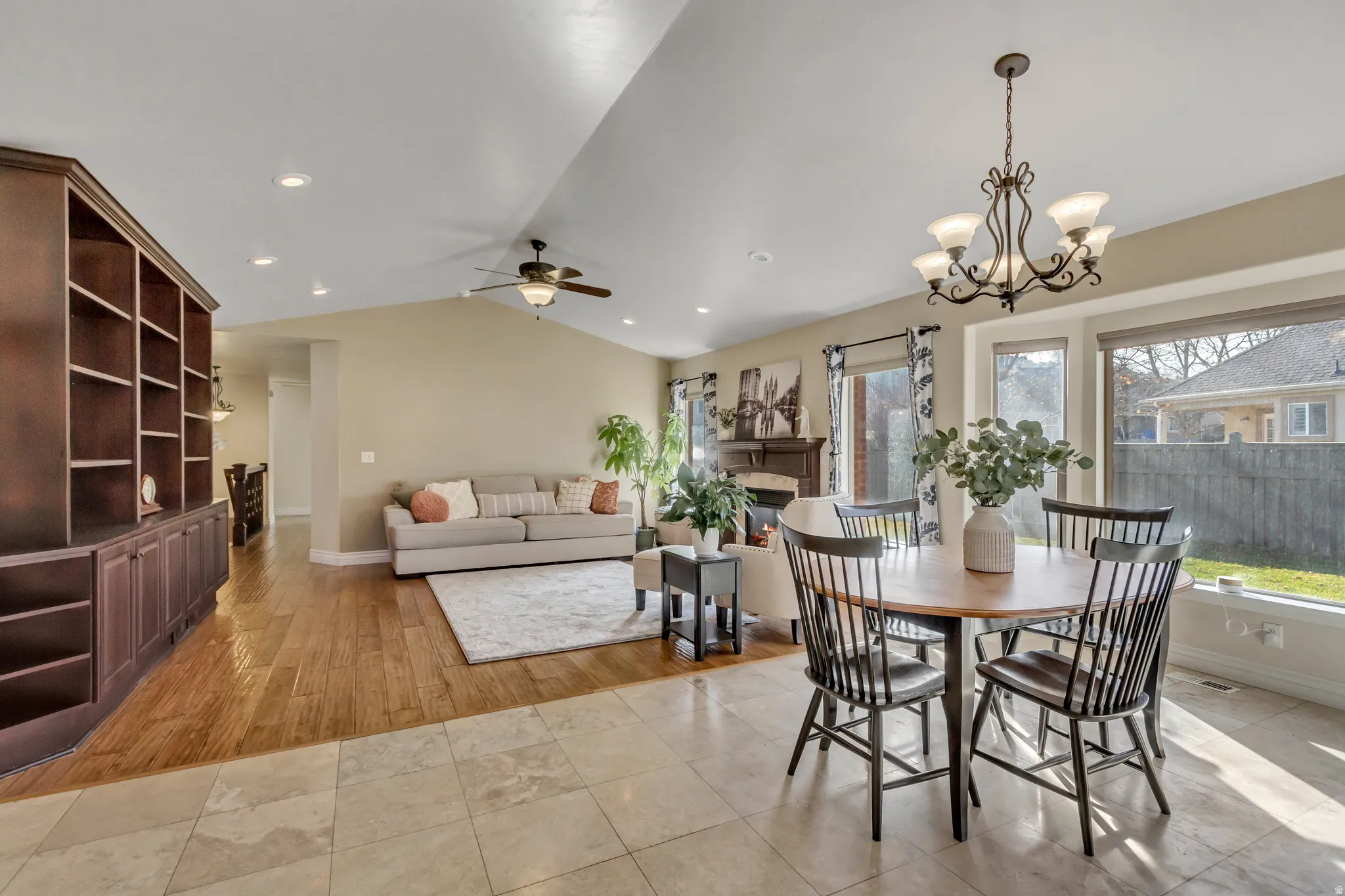 Dining area with a glass covered fireplace, vaulted ceiling, light tile patterned floors, a ceiling fan, and a chandelier
