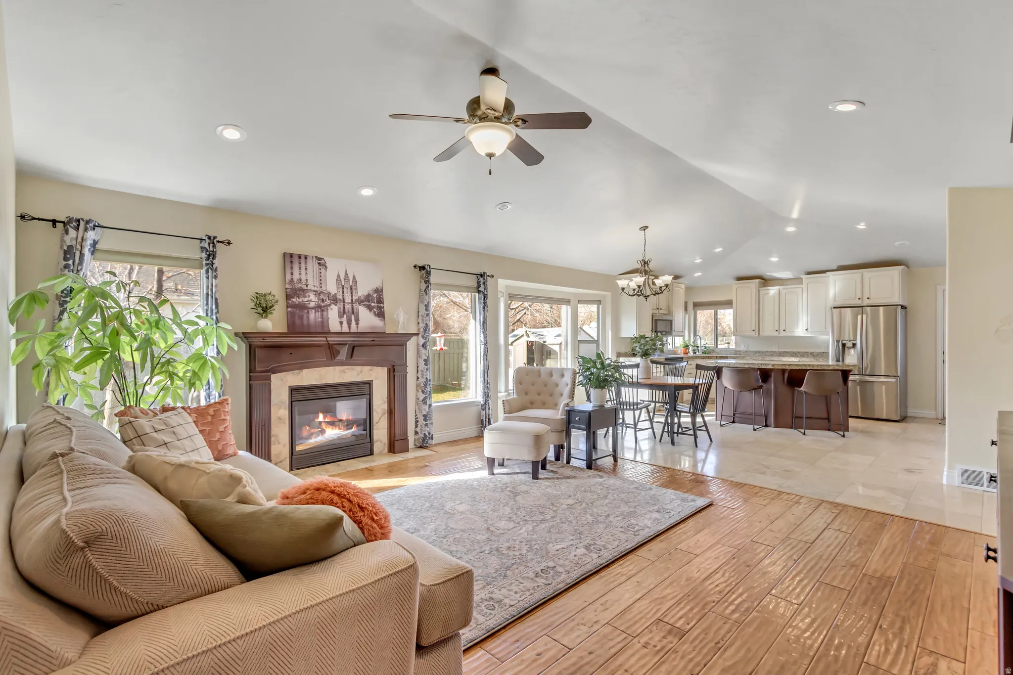 Living room featuring light wood-style flooring, vaulted ceiling, a chandelier, a premium fireplace, and ceiling fan
