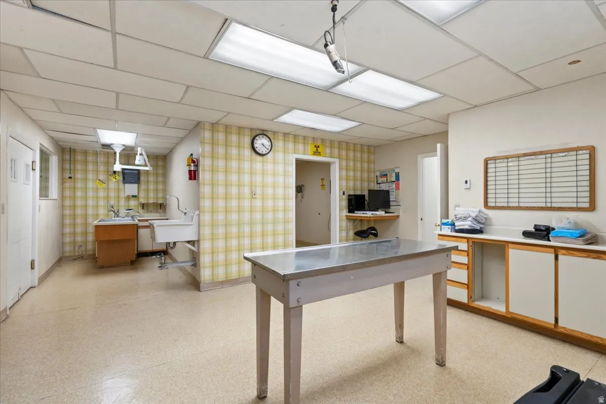 Home office with a paneled ceiling, wallpapered walls, and light floors