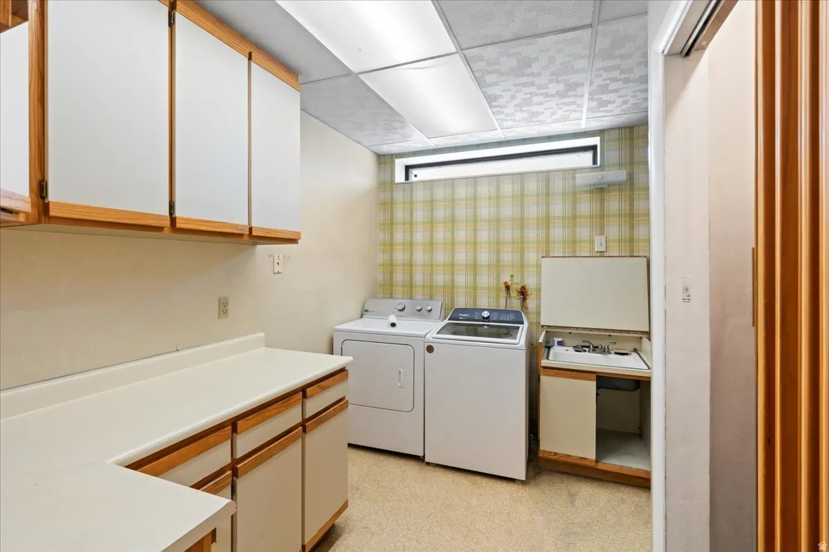 Laundry room featuring a drop ceiling, washing machine and clothes dryer, and cabinet space
