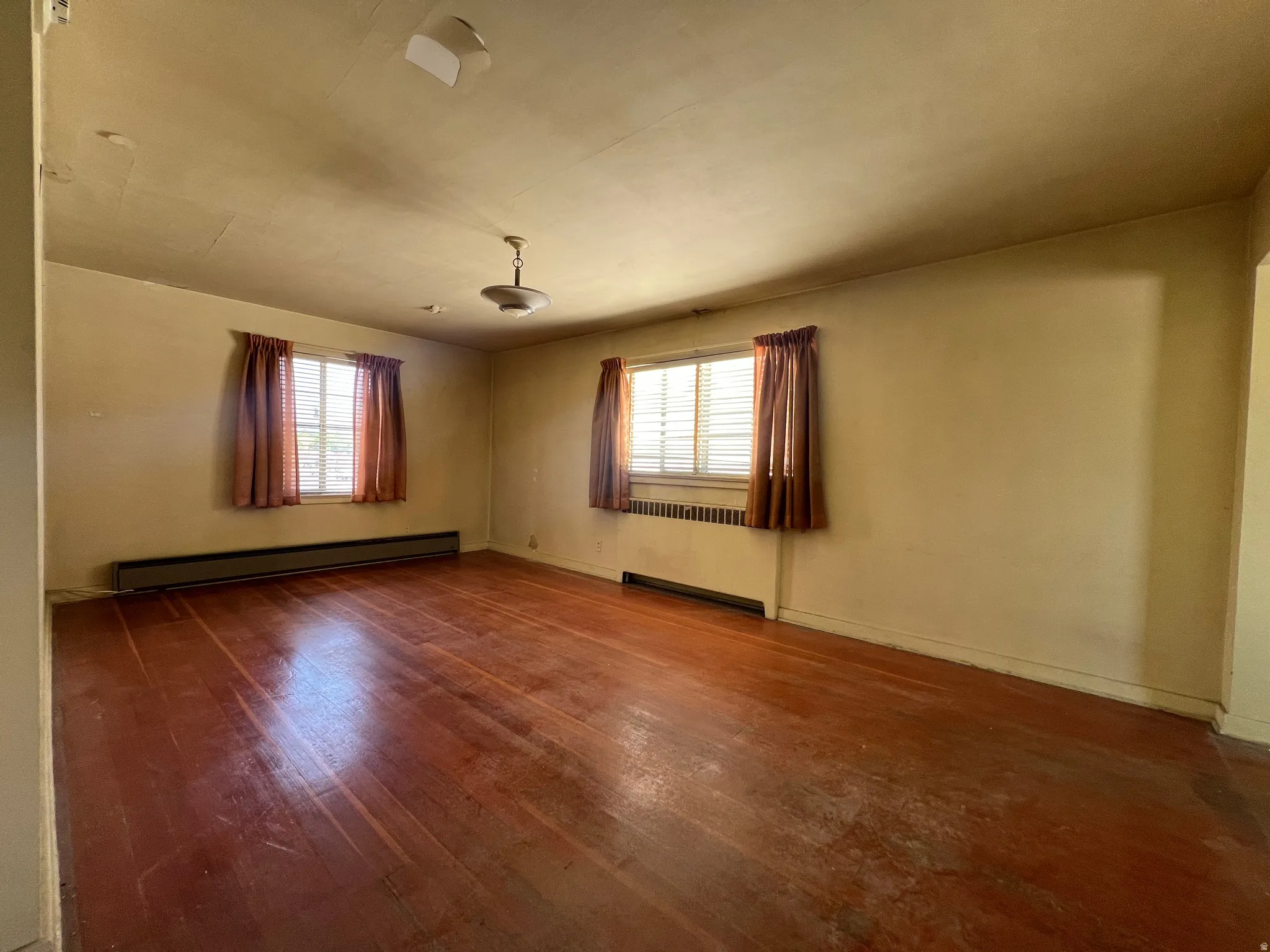 Empty room featuring healthy amount of natural light, a baseboard radiator, dark wood finished floors, and a baseboard heating unit