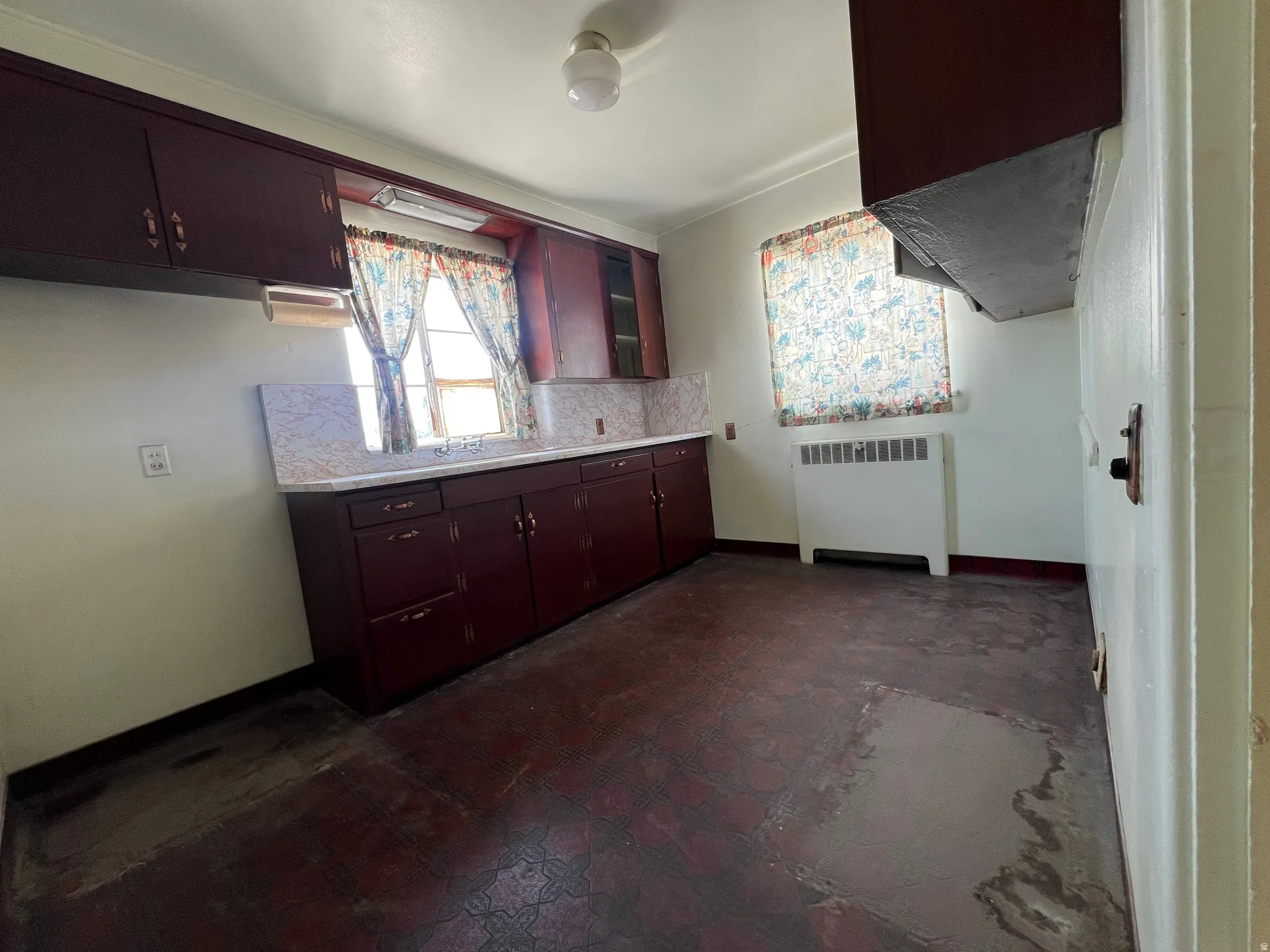 Kitchen featuring light countertops, radiator heating unit, dark flooring, and dark brown cabinets