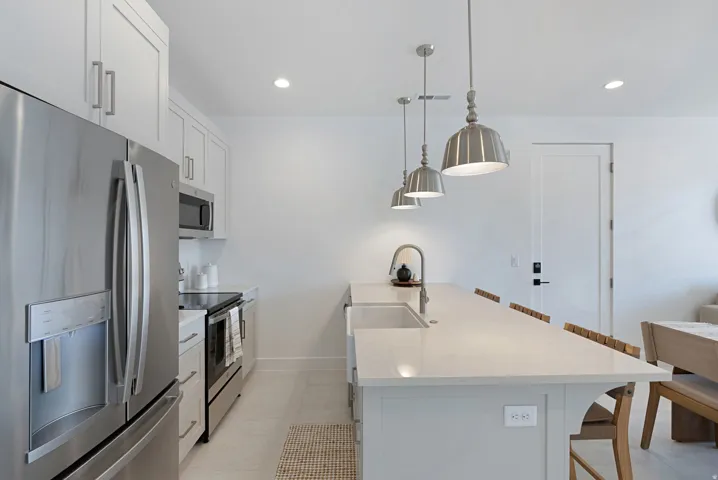 Kitchen featuring a breakfast bar, white cabinetry, appliances with stainless steel finishes, decorative light fixtures, and light stone counters