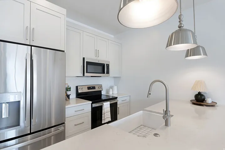 Kitchen with stainless steel appliances, white cabinets, light stone counters, and hanging light fixtures