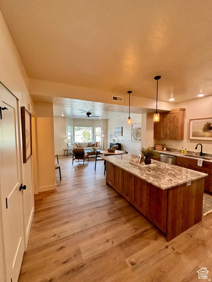 Kitchen with decorative light fixtures, open floor plan, light stone counters, light wood-style floors, and a kitchen island