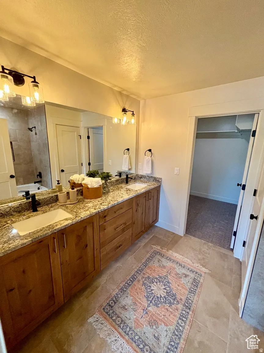 Bathroom with a textured ceiling, a tile shower, double vanity, and a walk in closet
