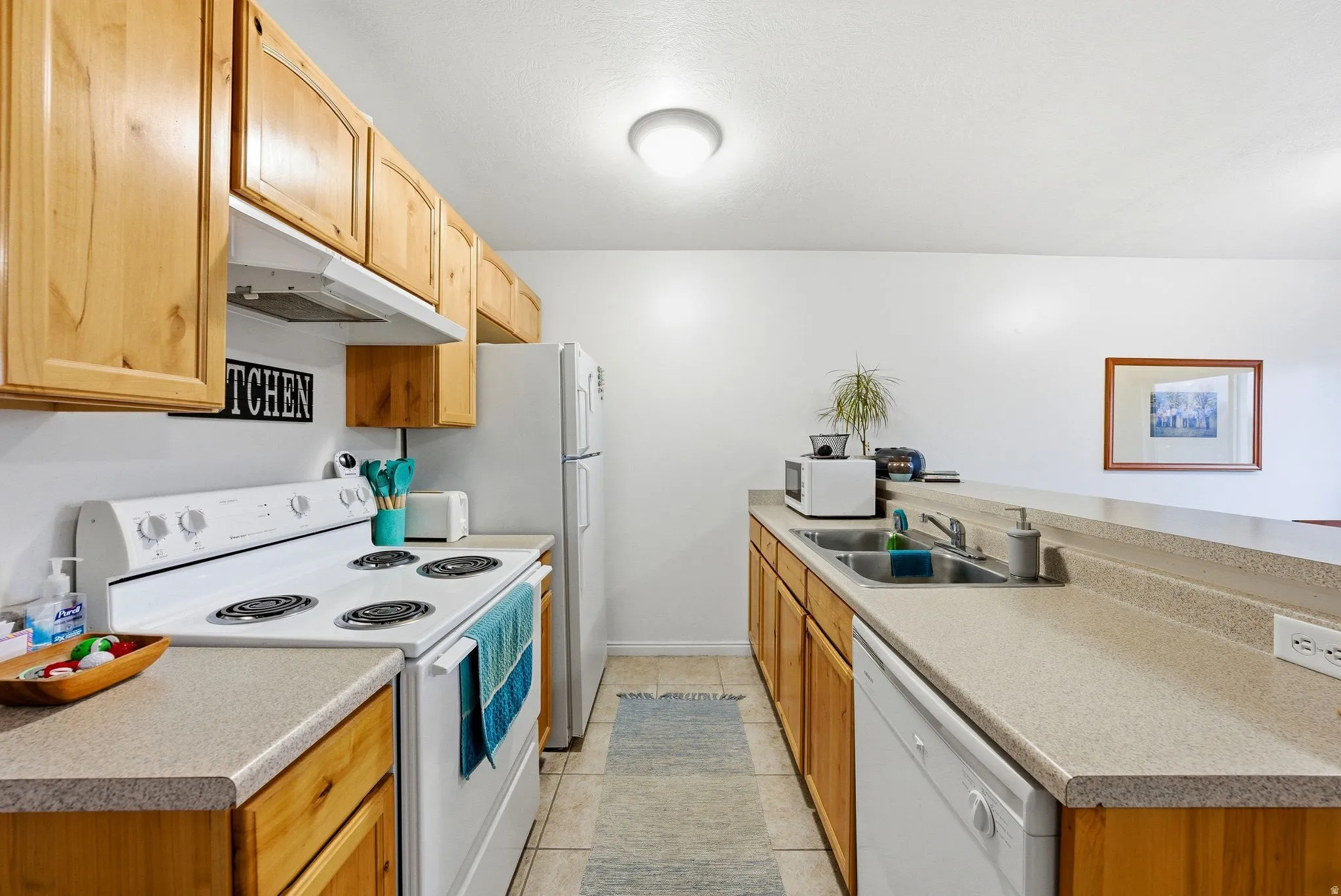 Kitchen with white appliances, a peninsula, under cabinet range hood, light countertops, and light tile patterned flooring