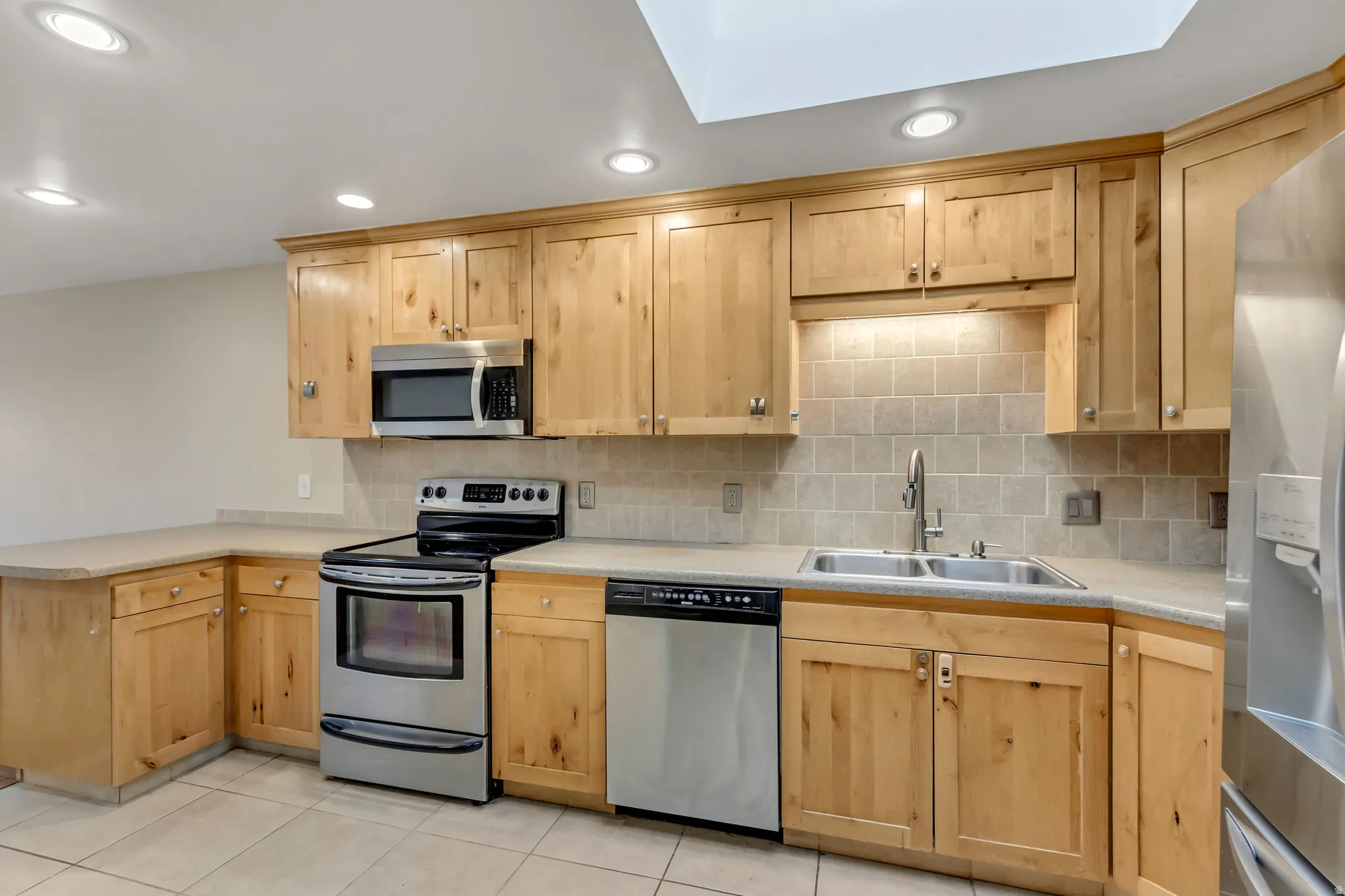 Kitchen featuring appliances with stainless steel finishes, light brown cabinetry, light countertops, a skylight, and recessed lighting