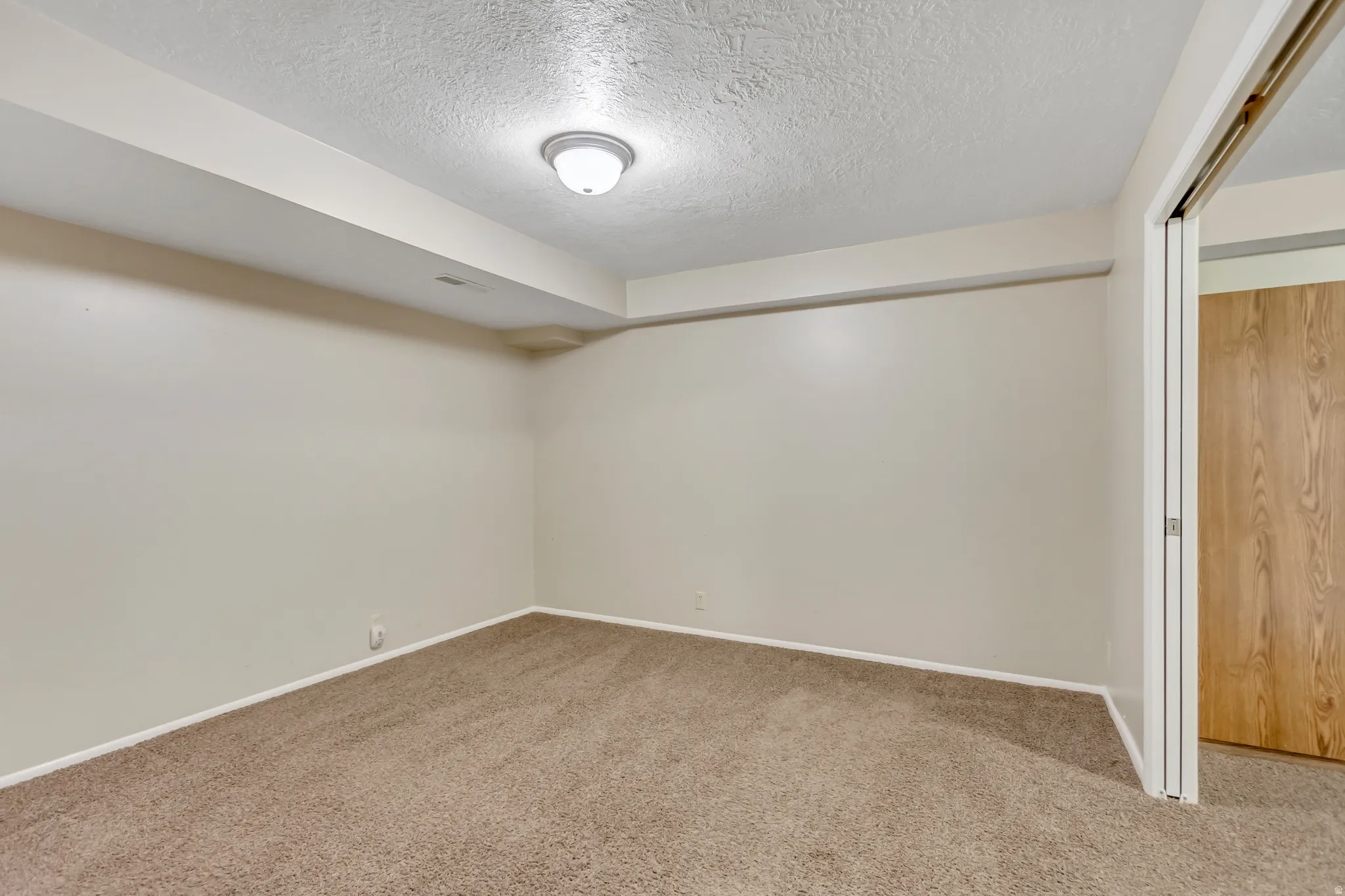Carpeted empty room with a textured ceiling and baseboards