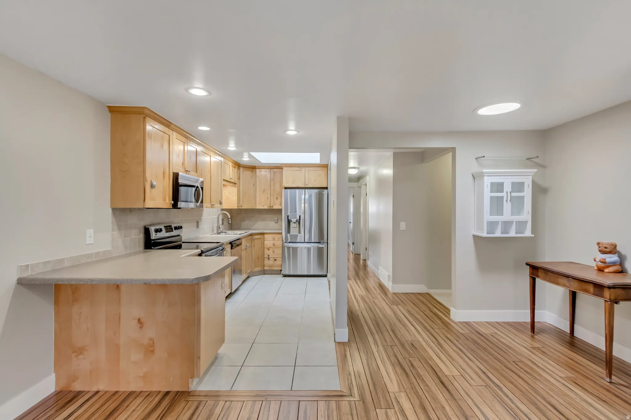 Kitchen featuring light brown cabinets, light countertops, appliances with stainless steel finishes, a peninsula, and decorative backsplash
