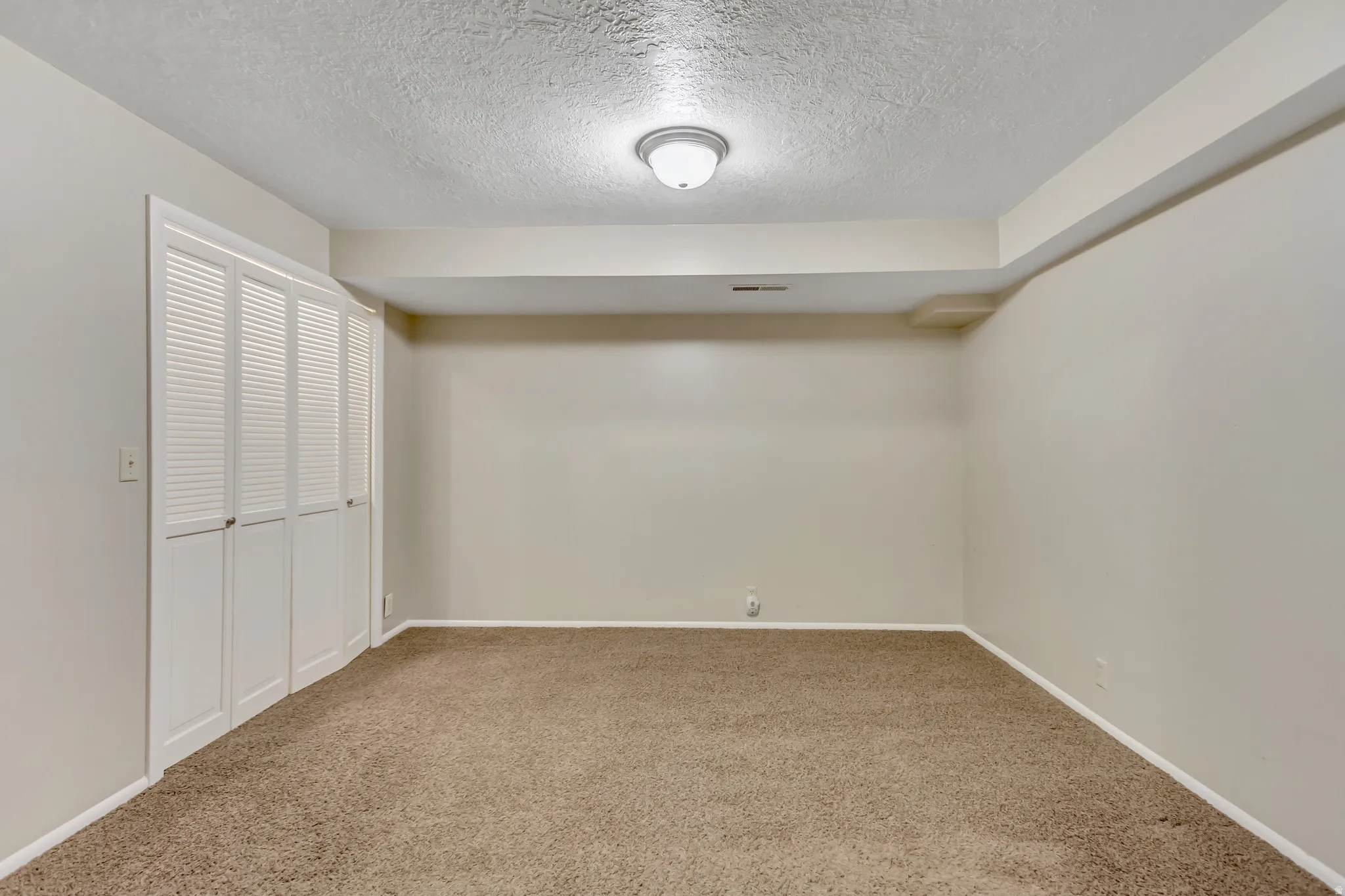 Unfurnished room with a textured ceiling, light colored carpet, and a closet