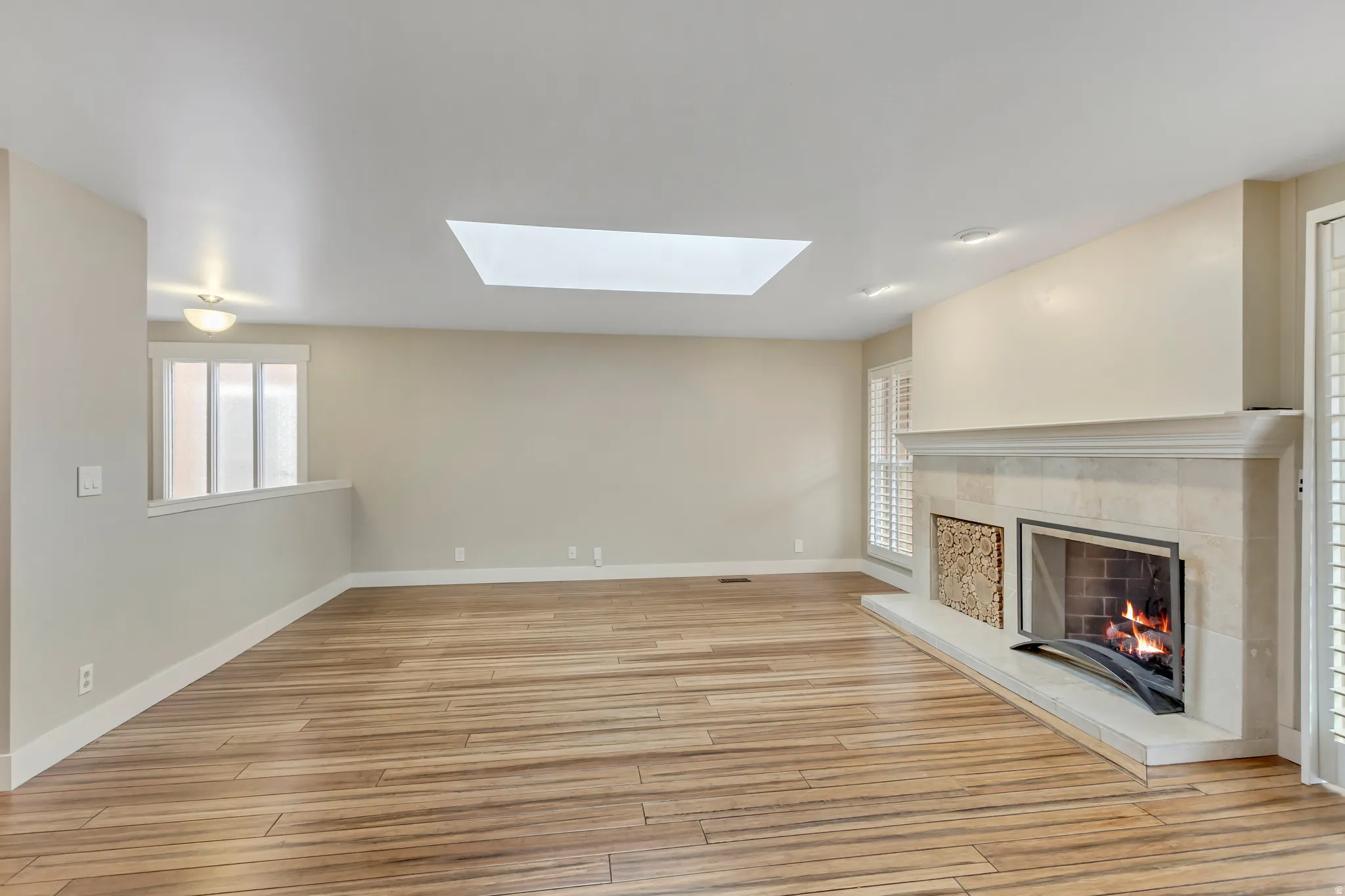 Unfurnished living room with a fireplace, light wood-type flooring, and a skylight