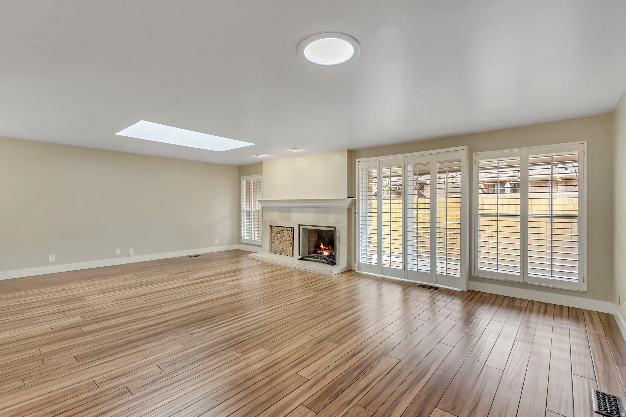 Unfurnished living room with a skylight, light wood finished floors, and a tiled fireplace