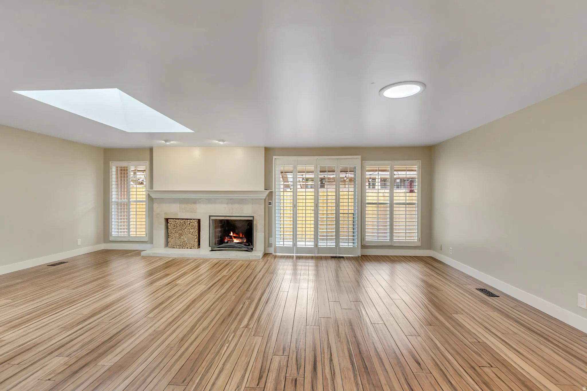 Unfurnished living room featuring a skylight, light wood-type flooring, healthy amount of natural light, and a tiled fireplace