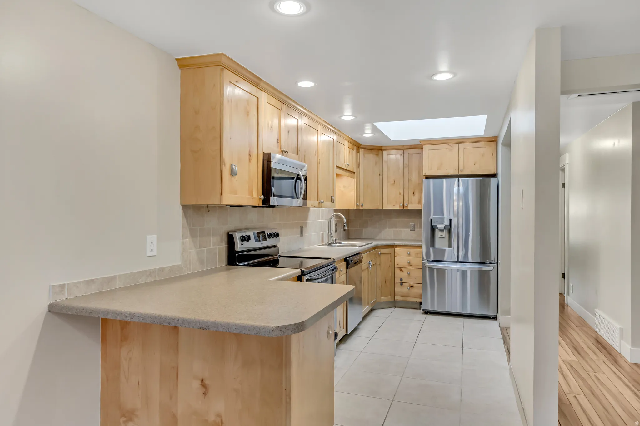Kitchen with light brown cabinetry, stainless steel appliances, tasteful backsplash, a peninsula, and light countertops
