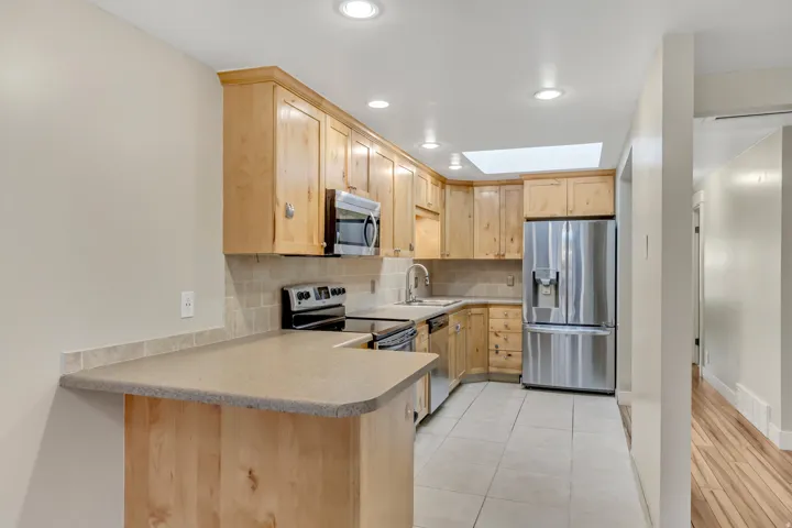 Kitchen with light brown cabinetry, stainless steel appliances, tasteful backsplash, a peninsula, and light countertops