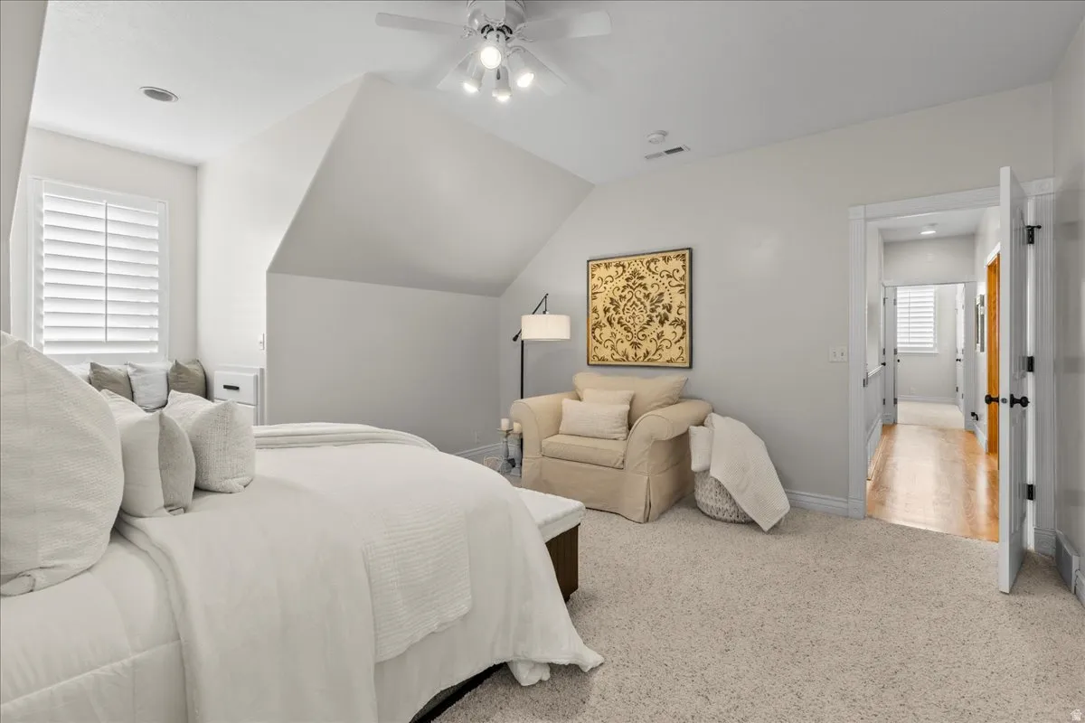 Carpeted bedroom with ceiling fan and vaulted ceiling