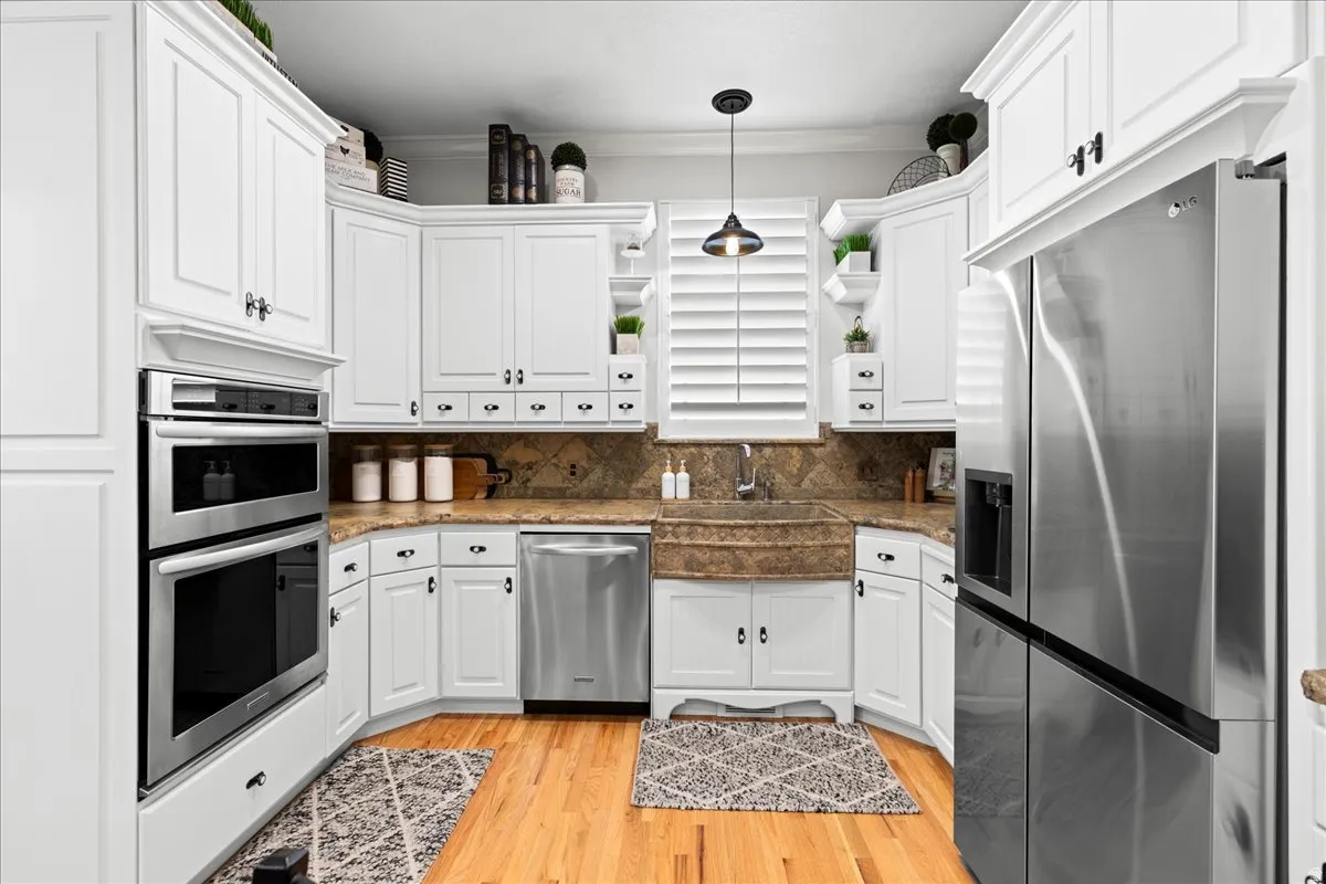 Kitchen with stainless steel appliances, white cabinetry, crown molding, light wood-style flooring, and hanging light fixtures