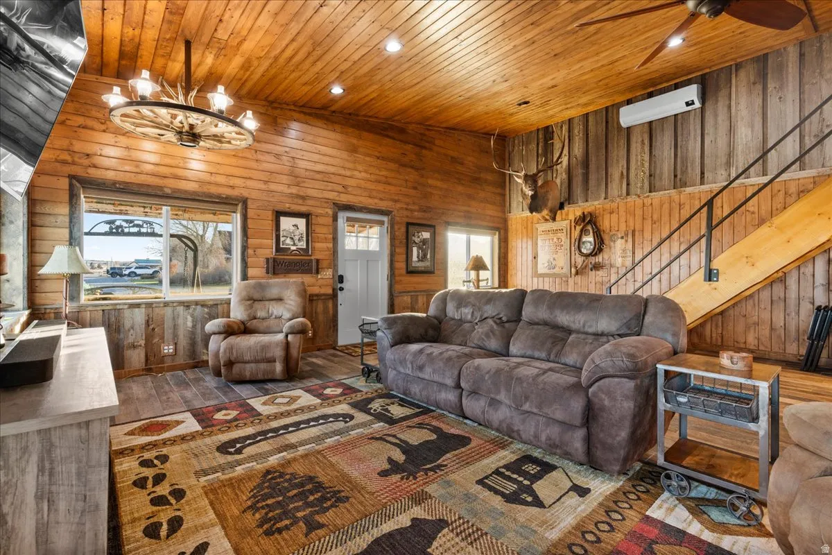 Living area with wooden walls, wood ceiling, a ceiling fan, healthy amount of natural light, and stairs