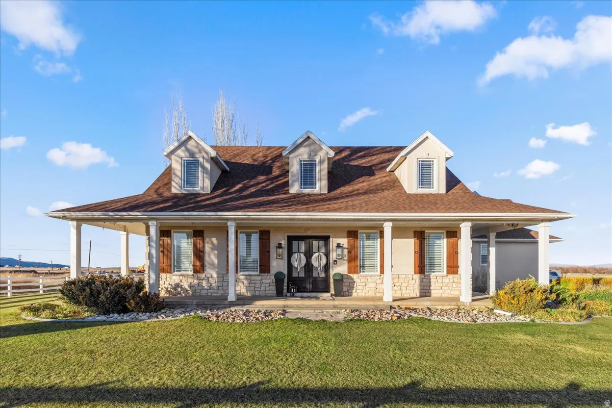 Farmhouse inspired home with a porch, a front lawn, stone siding, and stucco siding