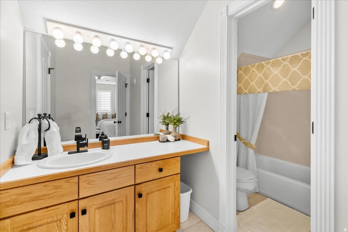 Full bathroom with vanity, lofted ceiling, shower / tub combo with curtain, light tile patterned flooring, and connected bathroom