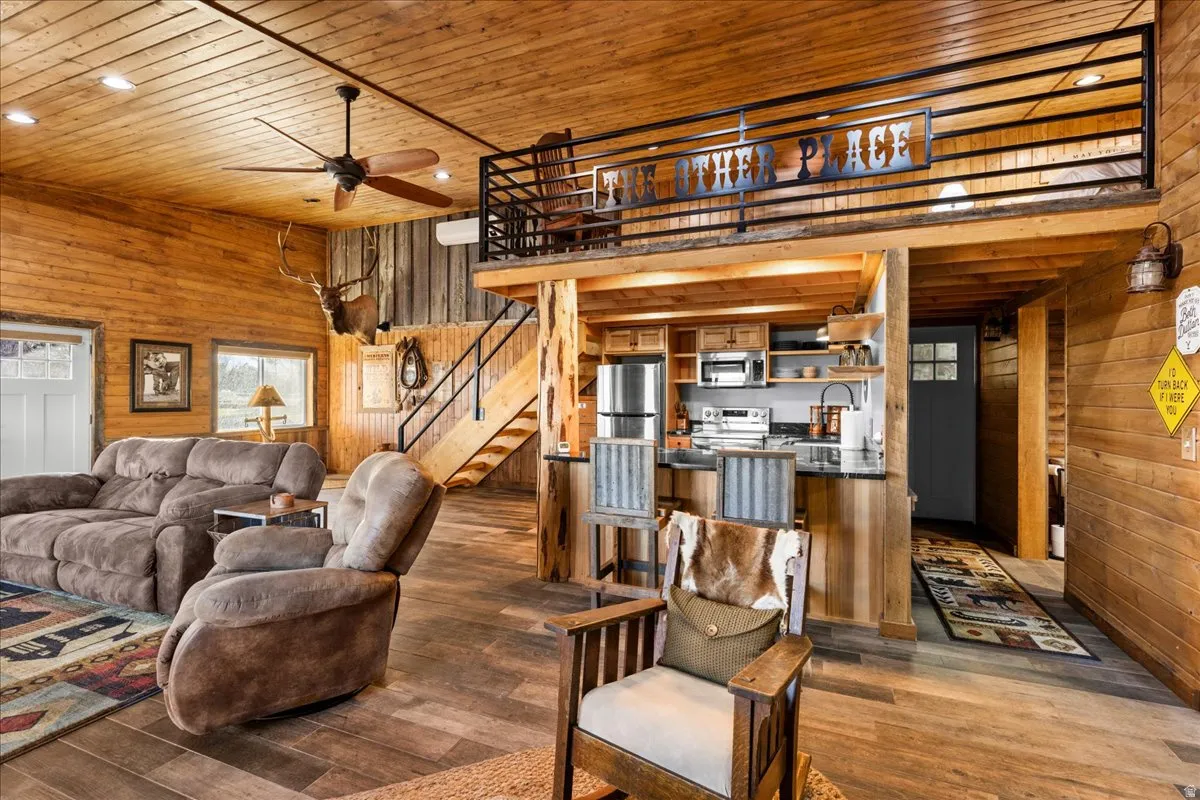 Living room featuring wood walls, wooden ceiling, dark wood finished floors, stairway, and a ceiling fan