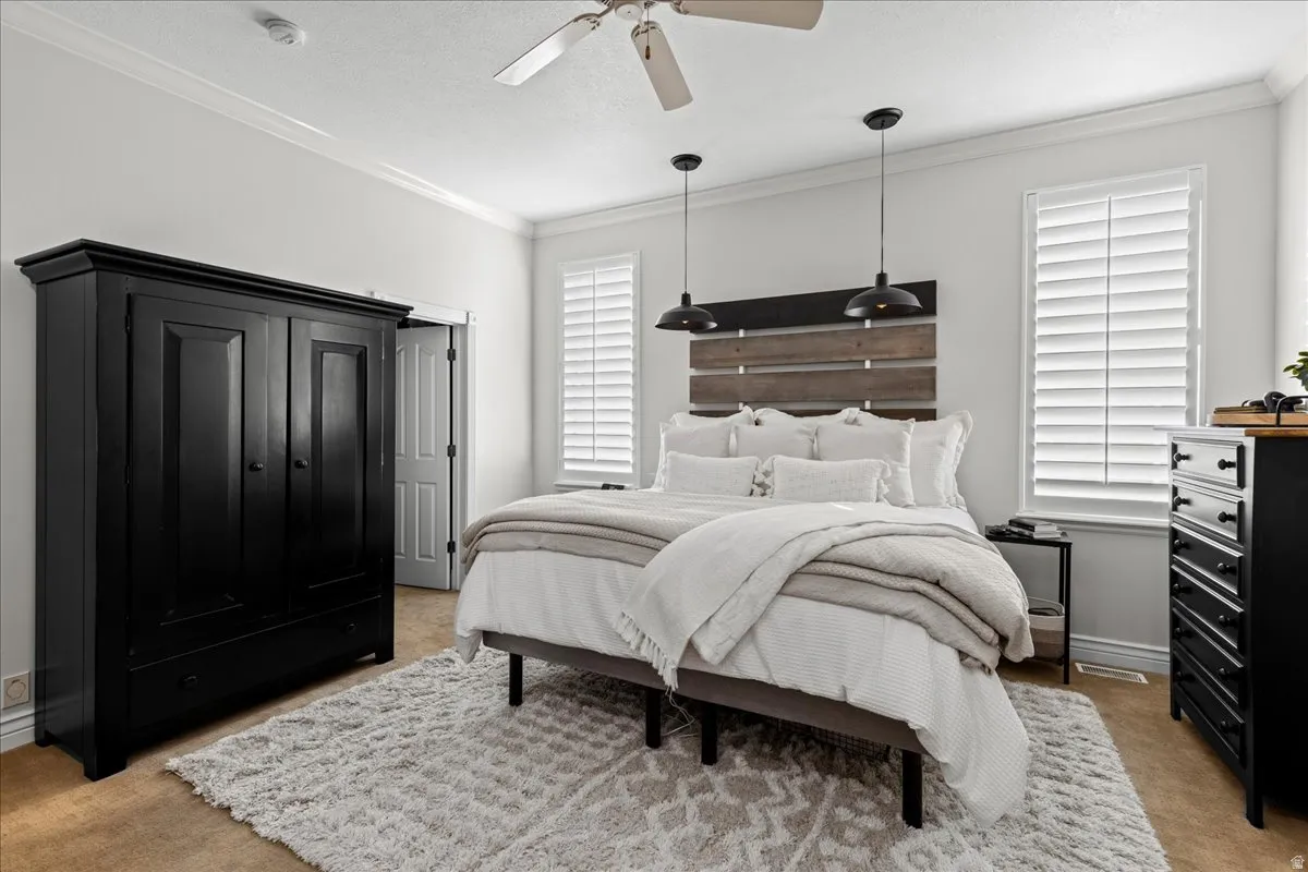 Bedroom with light colored carpet, crown molding, and ceiling fan
