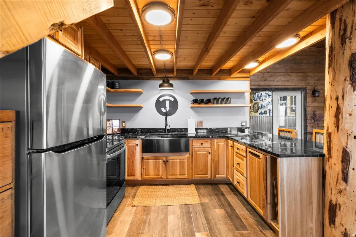 Kitchen featuring freestanding refrigerator, dark stone counters, a peninsula, open shelves, and light wood-type flooring