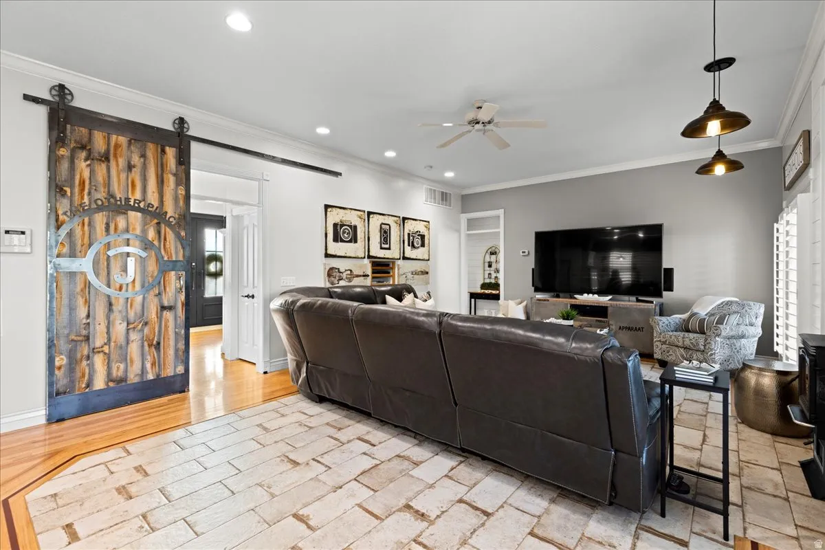 Living room featuring crown molding, ceiling fan, a barn door, and recessed lighting