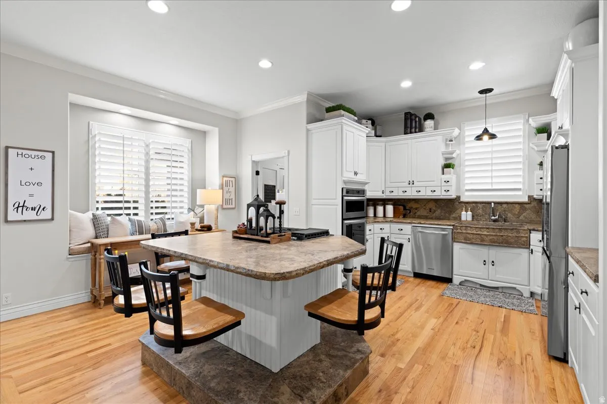 Kitchen featuring open shelves, white cabinetry, hanging light fixtures, a kitchen bar, and ornamental molding