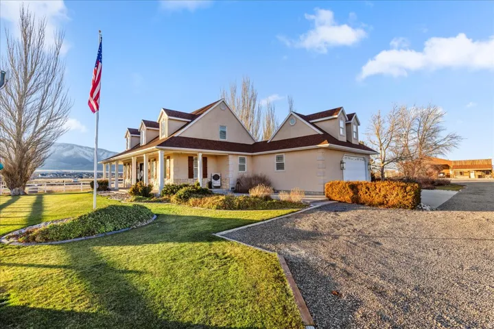 View of front facade featuring covered porch, stucco siding, a front lawn, a garage, and stone siding