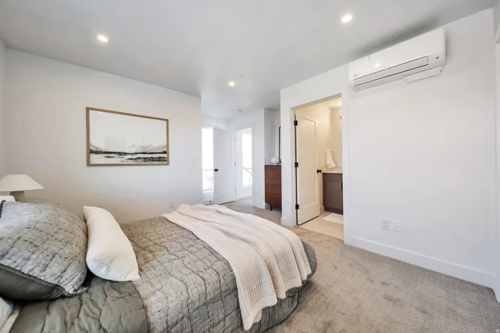 Bedroom featuring an AC wall unit, light carpet, connected bathroom, and recessed lighting