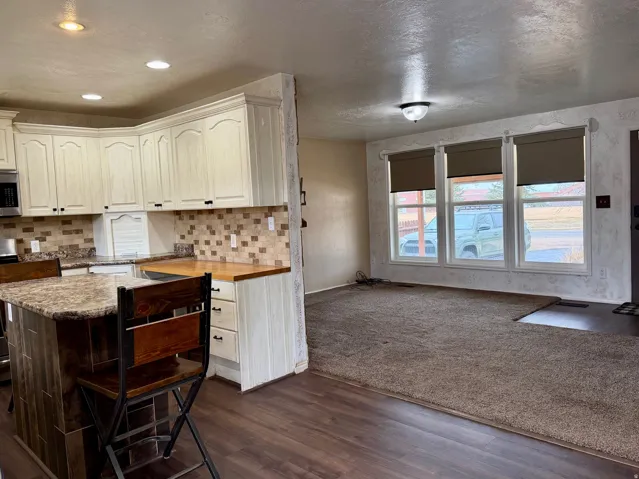 Kitchen with butcher block countertops, dark wood-style floors, stainless steel appliances, decorative backsplash, and white cabinetry