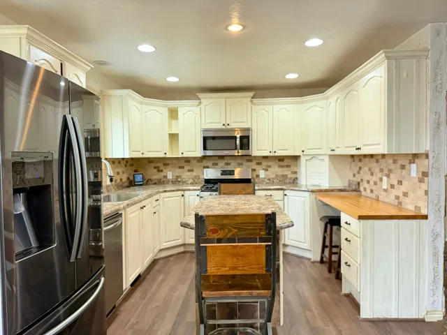Kitchen featuring stainless steel appliances, dark wood-style flooring, light stone countertops, decorative backsplash, and open shelves