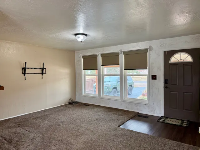 Foyer entrance featuring a textured ceiling, a textured wall, and dark carpet