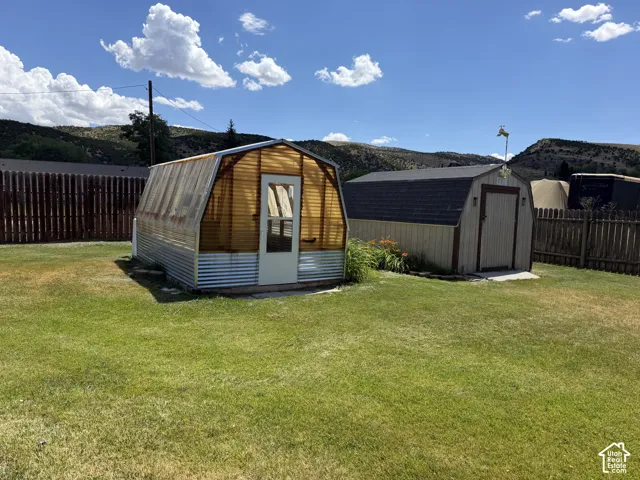 Expansive yard featuring a greenhouse with a corrugated metal base and a wood-paneled utility shed with an asphalt shingle roof
