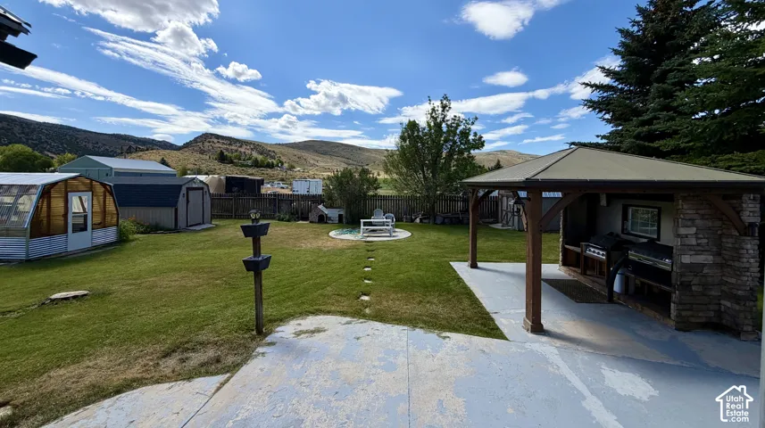 Expansive backyard featuring a stone and wood outdoor kitchen structure, concrete patio, and a greenhouse