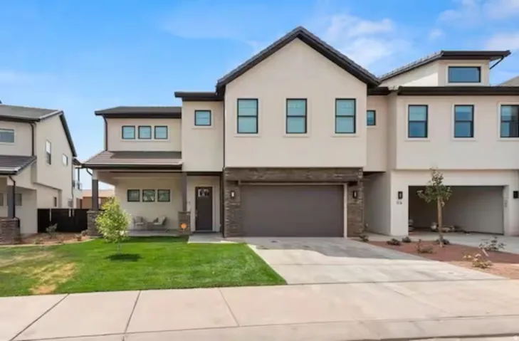 View of front facade with a front lawn, stucco siding, driveway, and a garage