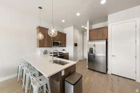 Kitchen with a kitchen bar, stainless steel appliances, pendant lighting, light countertops, and a peninsula