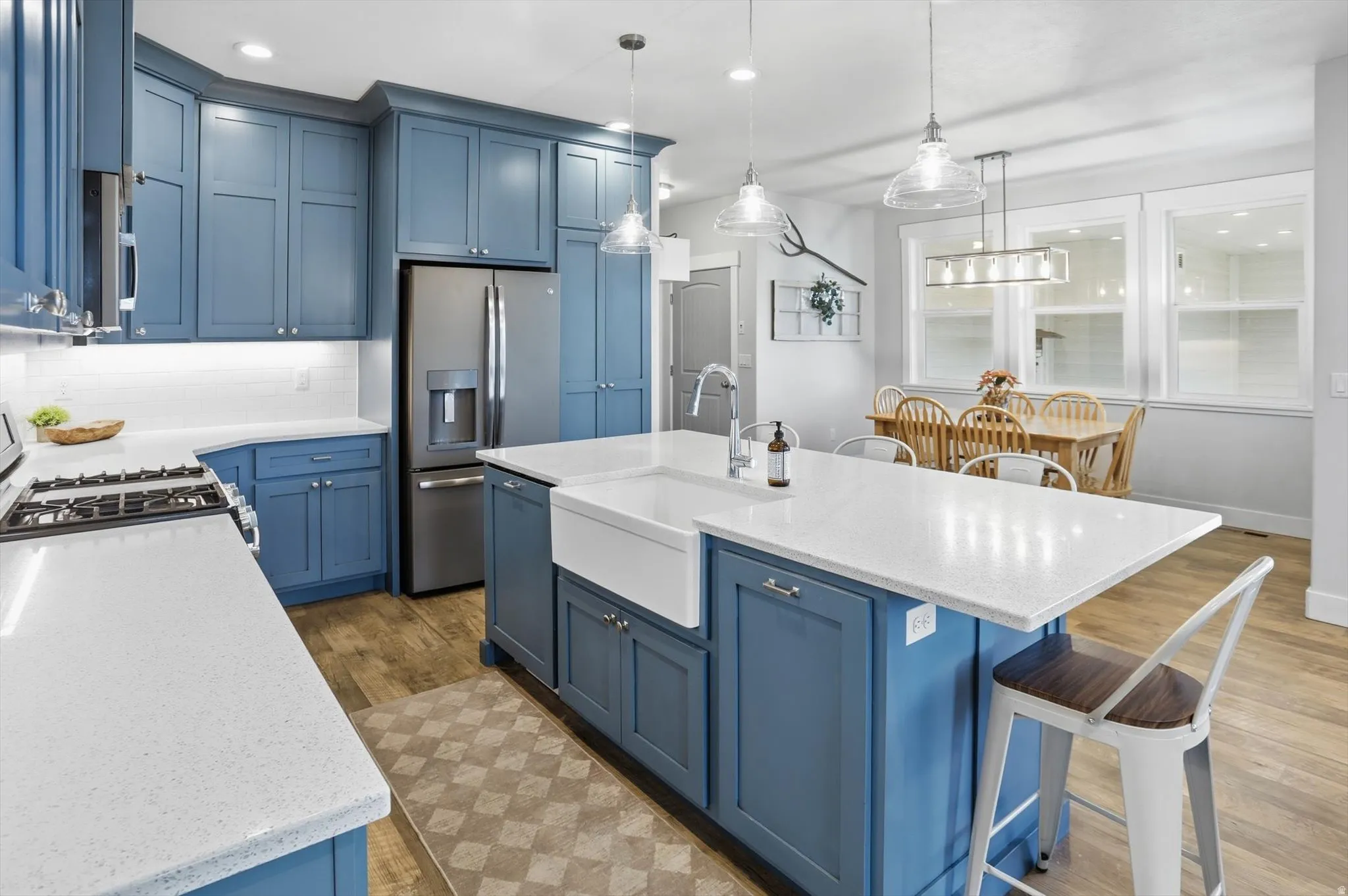 Kitchen featuring blue cabinets, a breakfast bar area, light stone countertops, a center island with sink, and pendant lighting