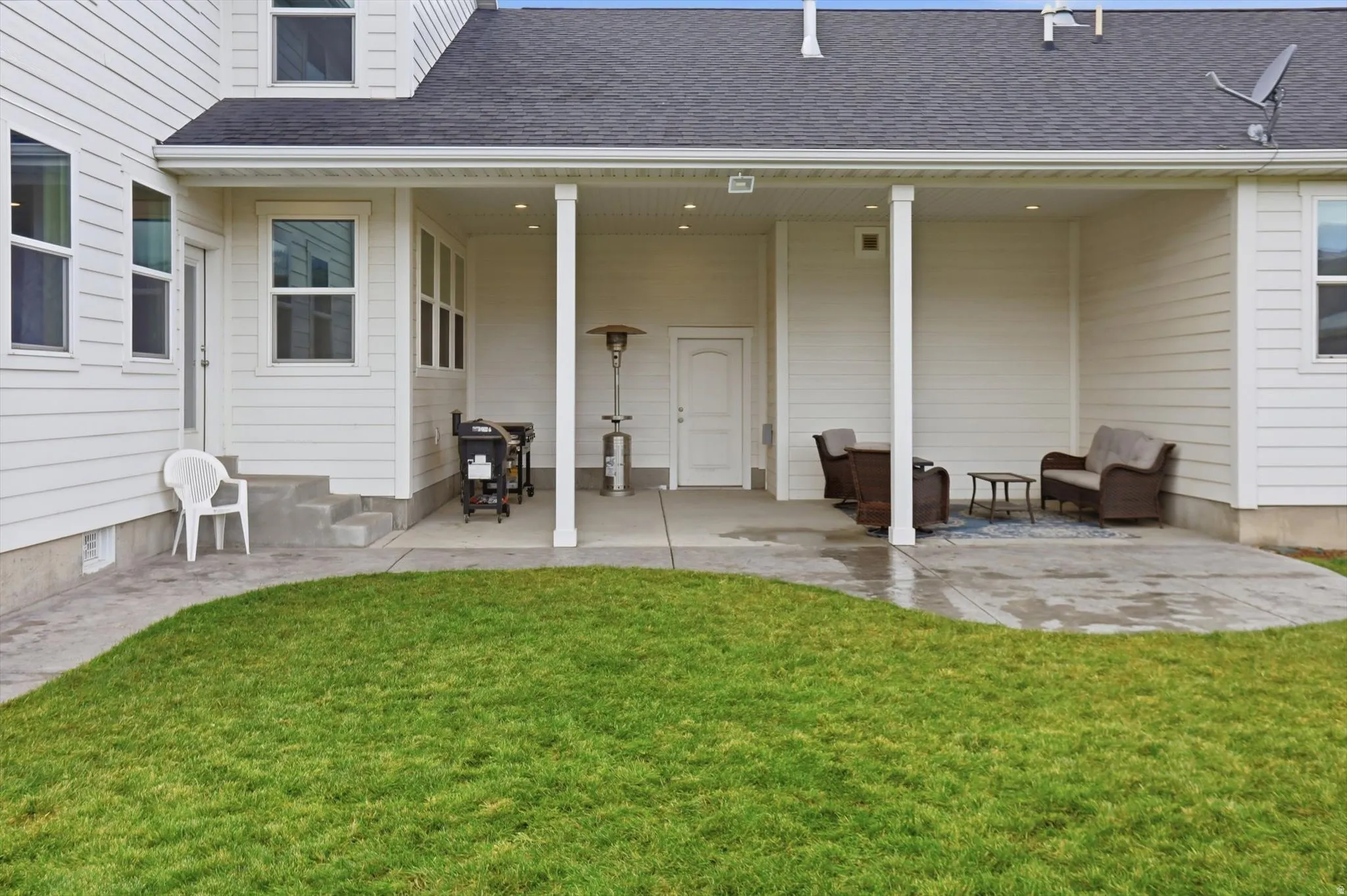 Rear view of house featuring a patio, a shingled roof, and a yard