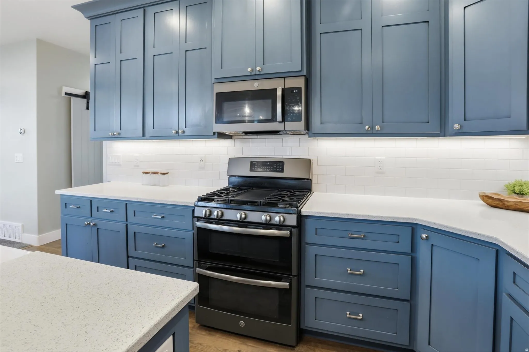 Kitchen featuring stainless steel appliances, blue cabinetry, light stone counters, and tasteful backsplash