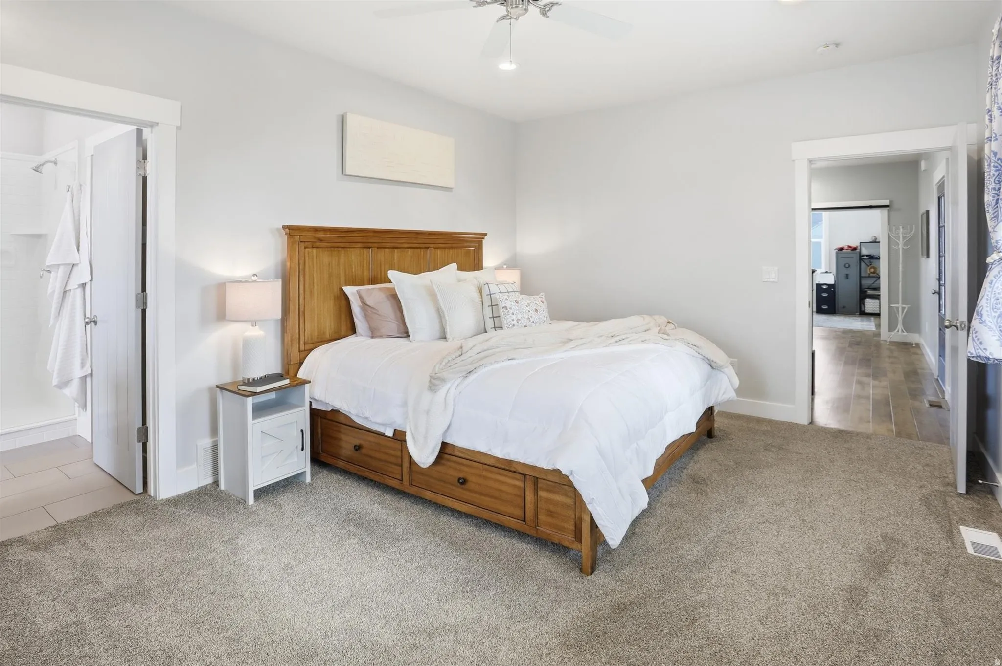main floor primary Bedroom with light carpet, ceiling fan, and connected bathroom