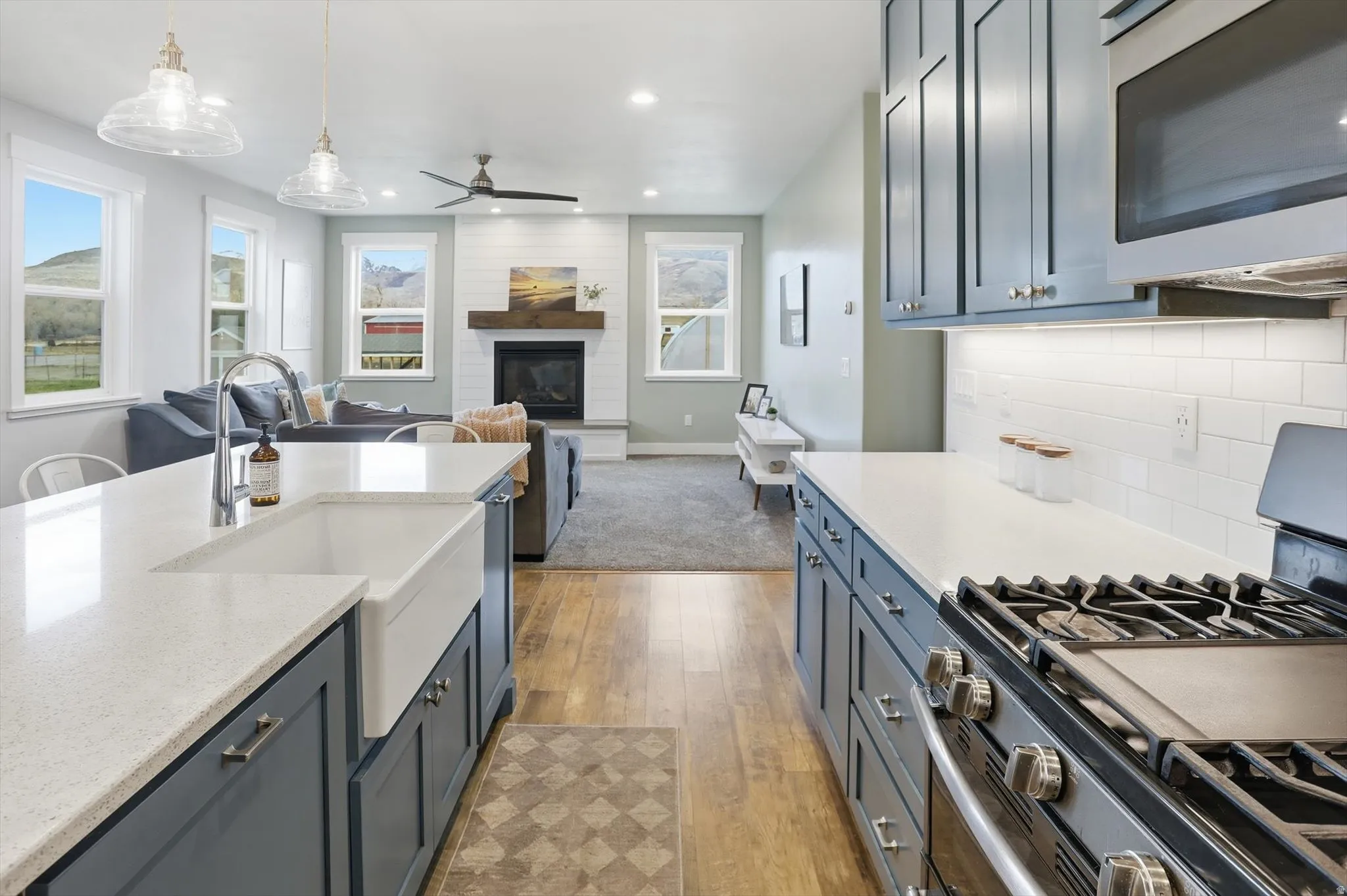 Kitchen with stainless steel appliances, light stone countertops, ceiling fan, light wood-type flooring, and a glass covered fireplace